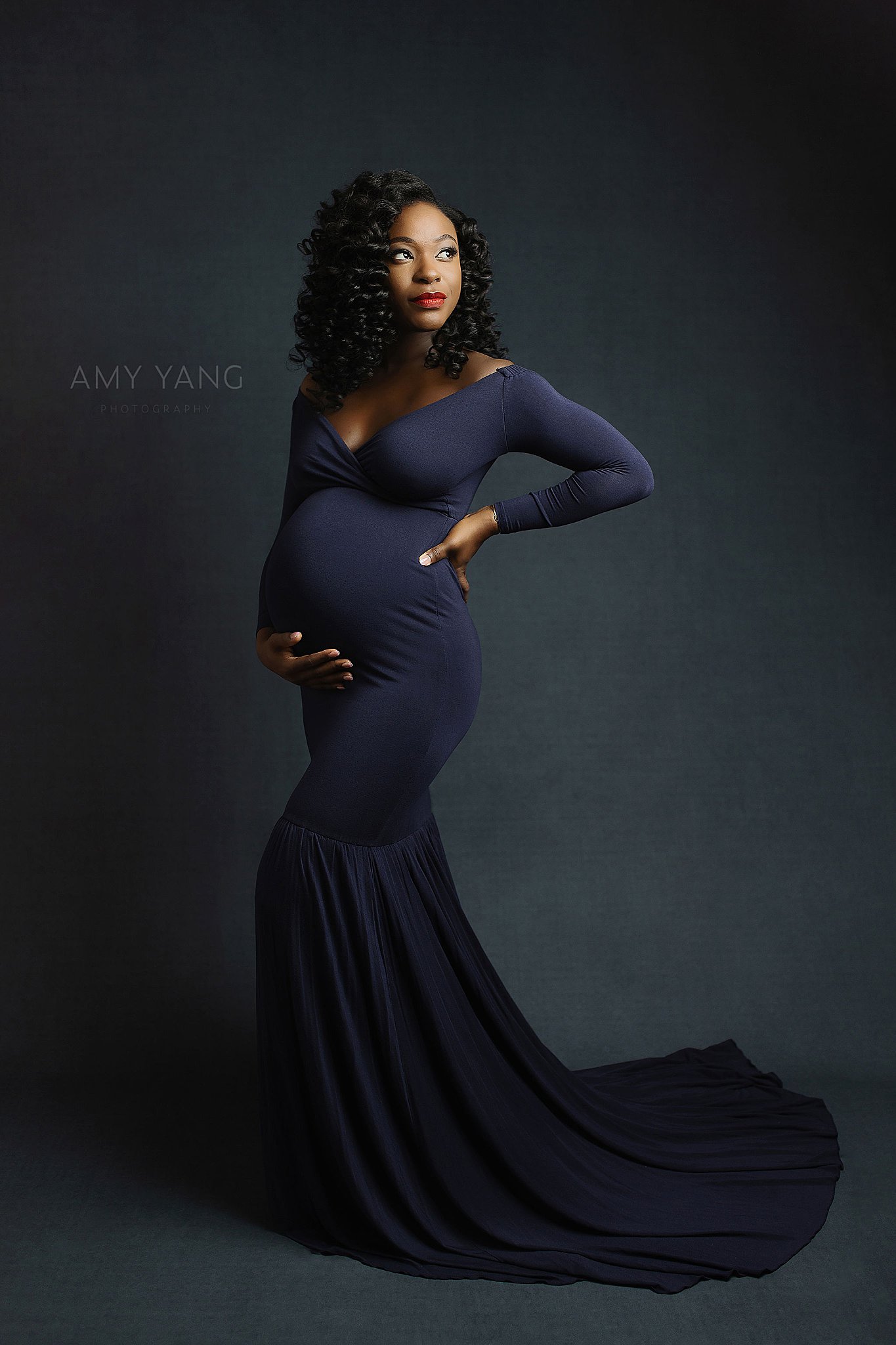 pregnant woman looks to side in studio as she holds her tummy by Charlottesville photographer