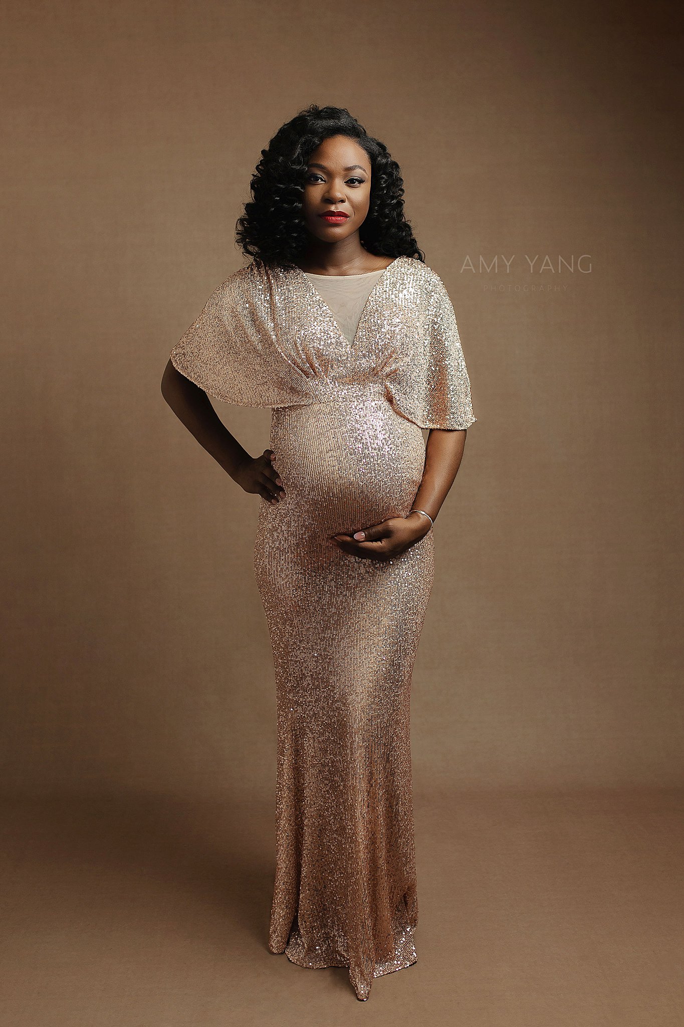 mother-to-be holds her growing belly in a sparkly gold gown during maternity session