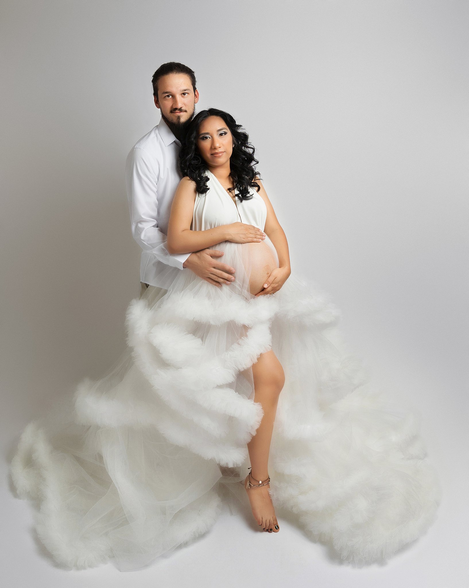 man wraps arms around mom's belly during studio maternity session