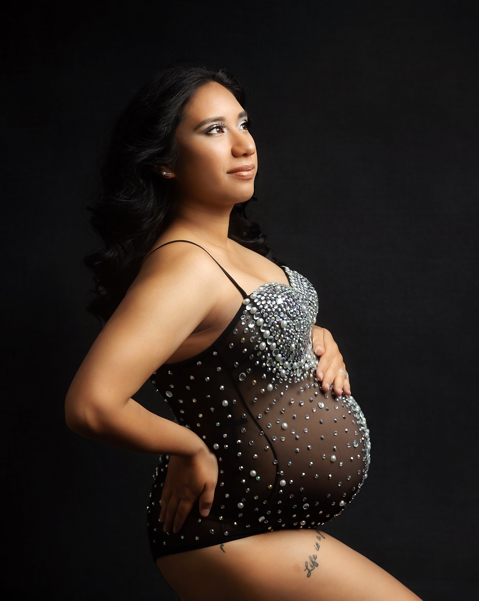 woman looks up to the side as she rests her hands on her hip and stomach by Amy Yang Photography