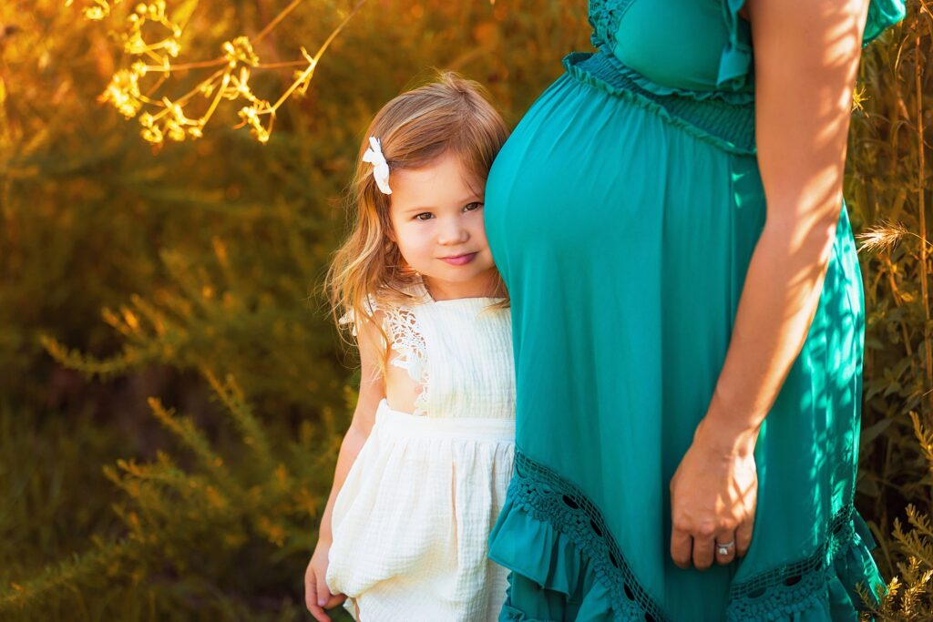 girl peeks out from behind her mom's baby bump by Charlottesville Photographer