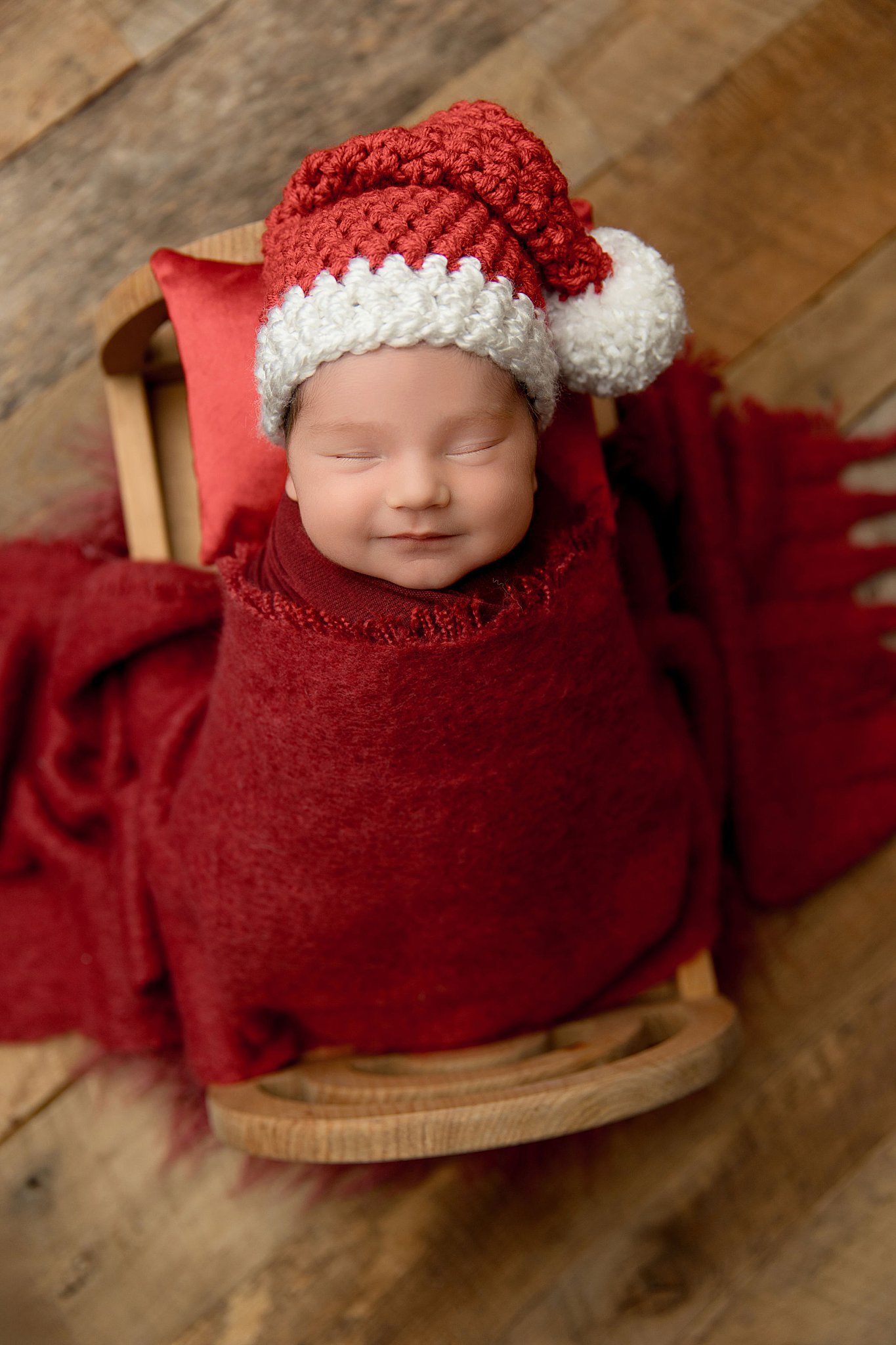 baby with santa hat lays on sled wrapped in red by Charlottesville photographer
