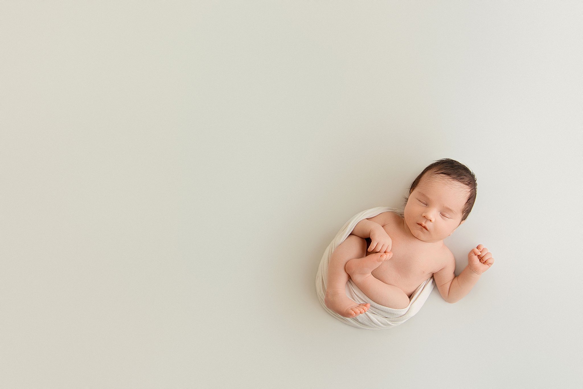 infant is wrapped in white and lays with arms and legs hanging out by Charlottesville photographer