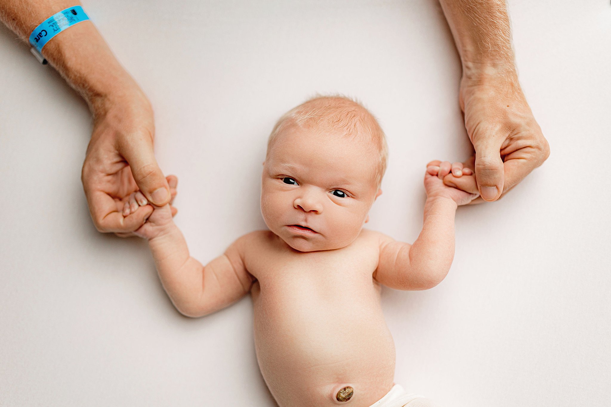 baby holds dad's hands during family newborn session 