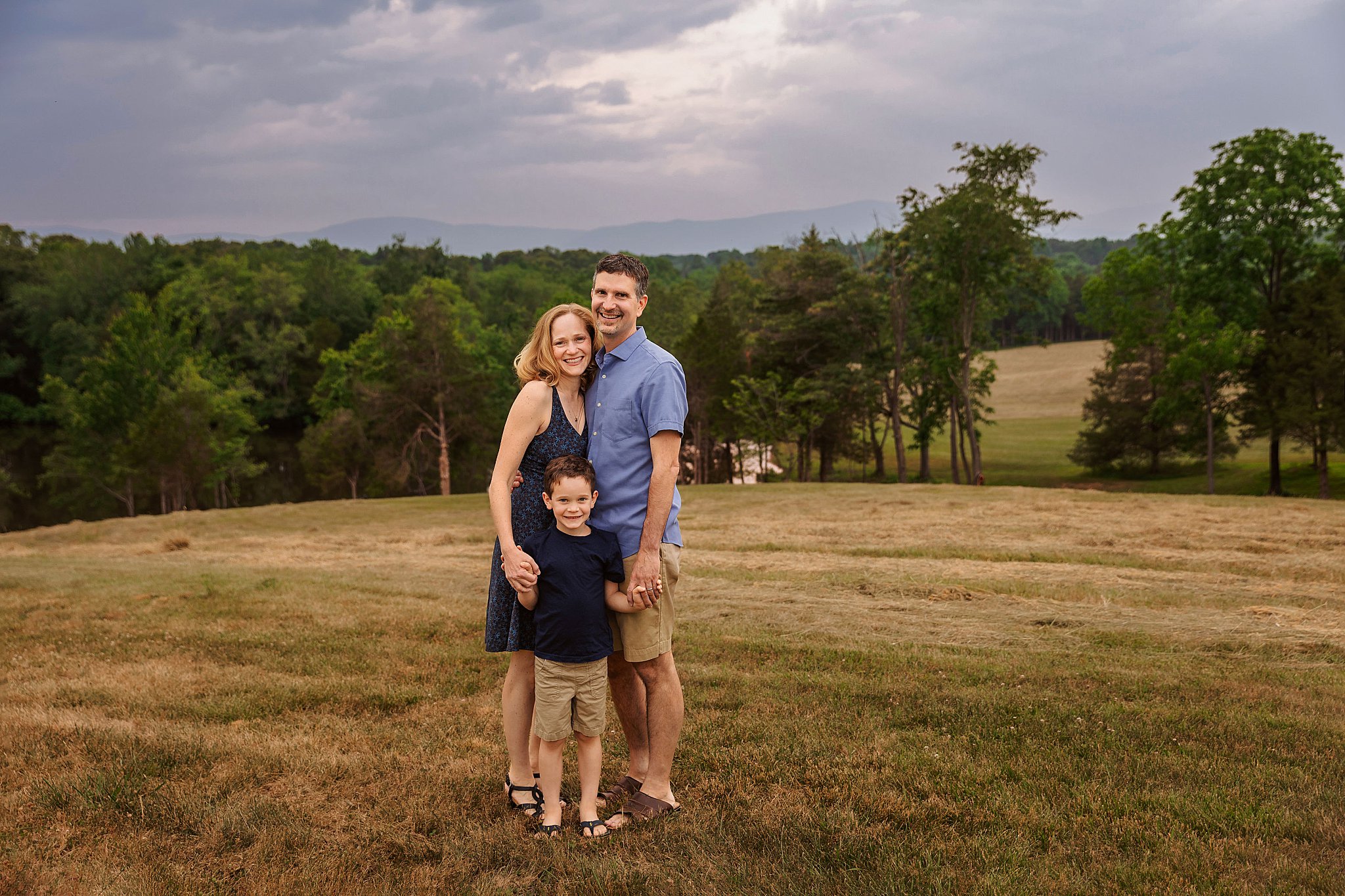 parents stand in field holding son's hand during simple family session