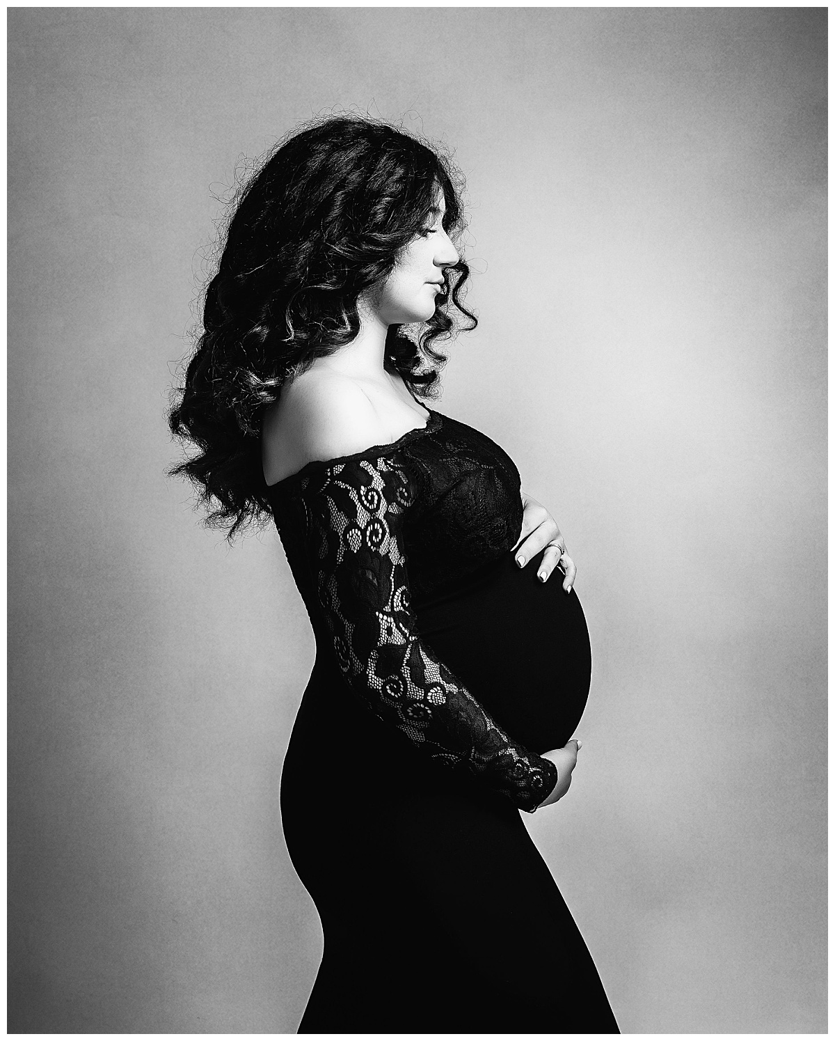 pregnant woman holds belly in long black gown by Charlottesville photographer