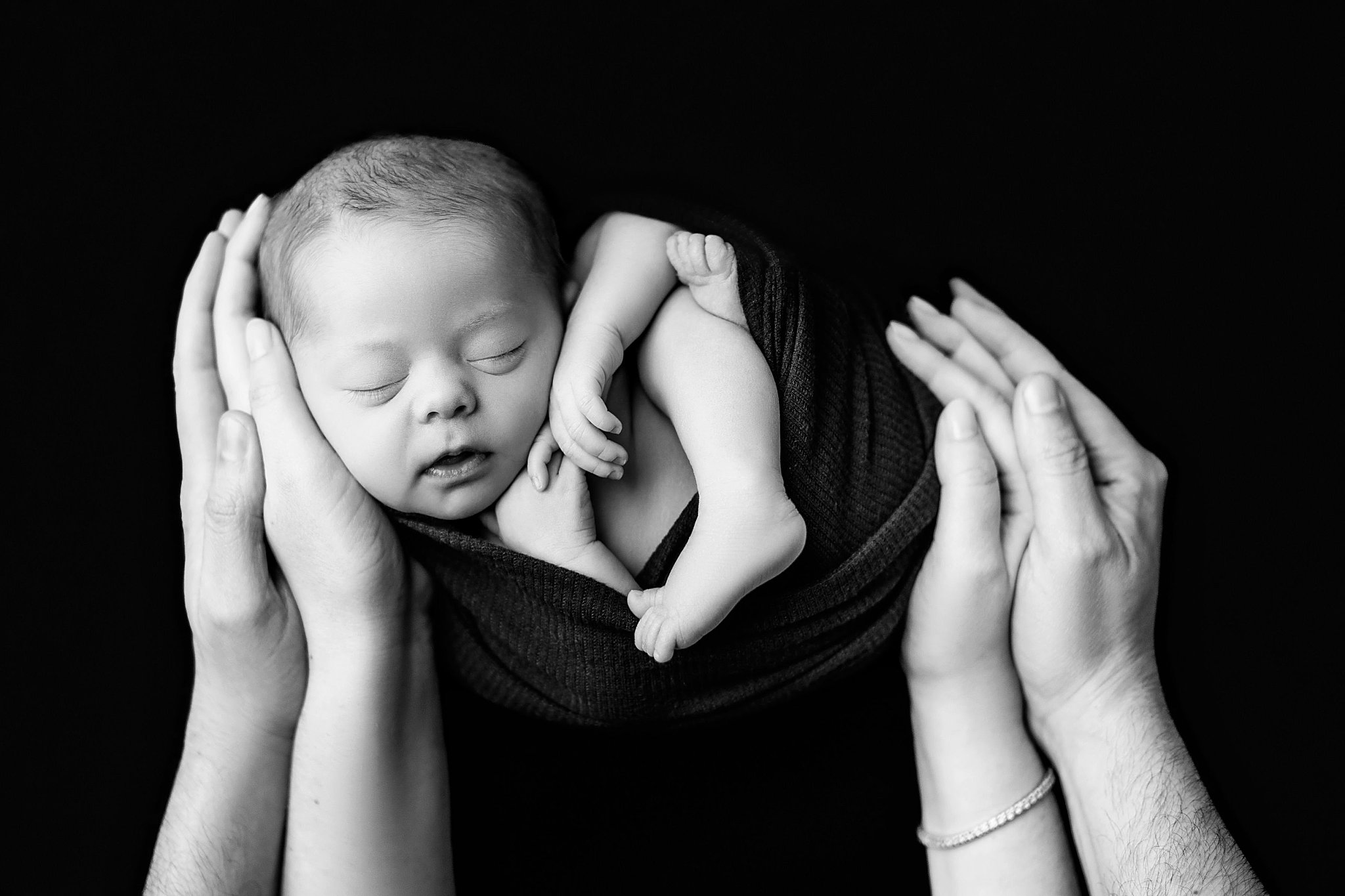 parents place hands around swaddled infant by Charlottesville photographer