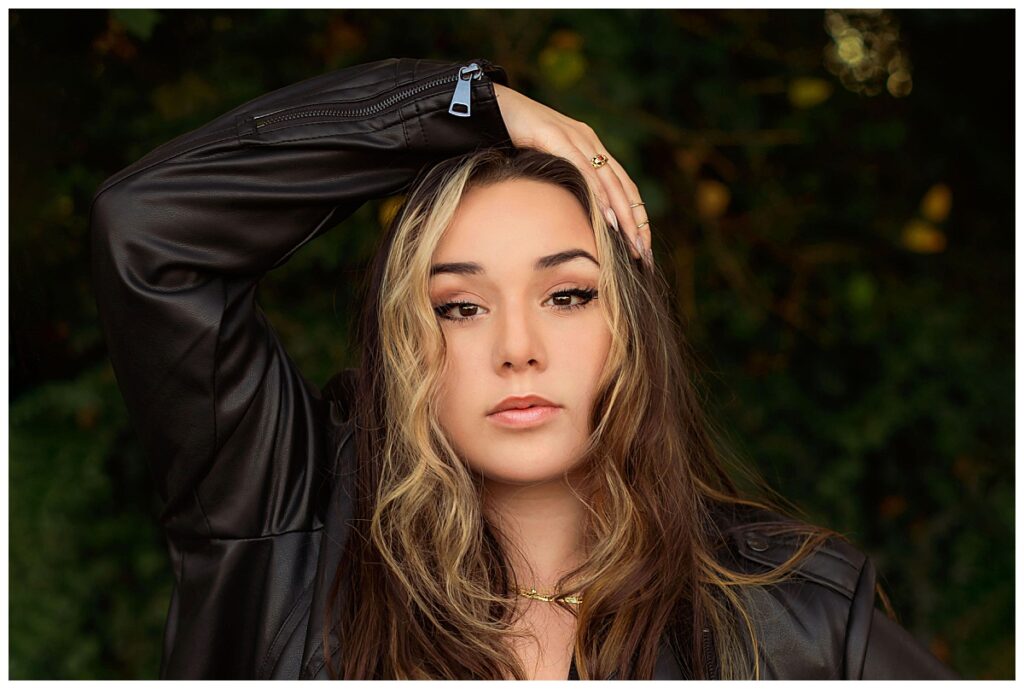Close-up senior portrait of a high school senior with highlighted hair wearing a black leather jacket, posing confidently outdoors during a senior session in Charlottesville, Virginia.
