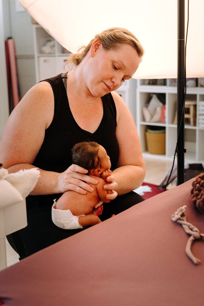 Behind the scenes newborn photography showing a photographer safely posing a newborn baby in Charlotteville newborn studio.