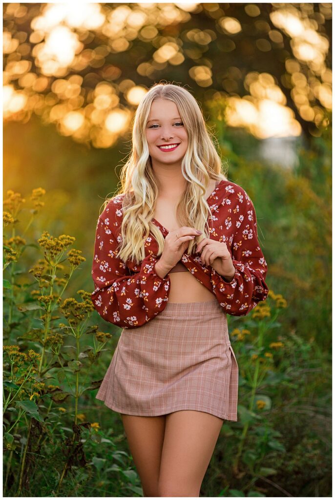 Senior portrait of a smiling blonde graduate surrounded by wildflowers at sunset in Charlottesville, VA.