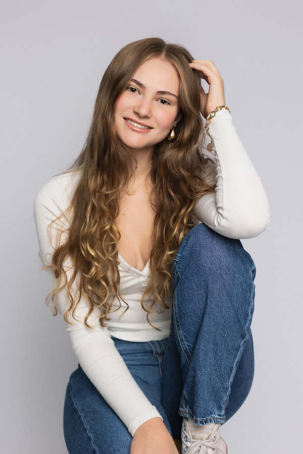 Studio portrait of a smiling high school senior in a white top and blue jeans by a Charlottesville senior photographer.