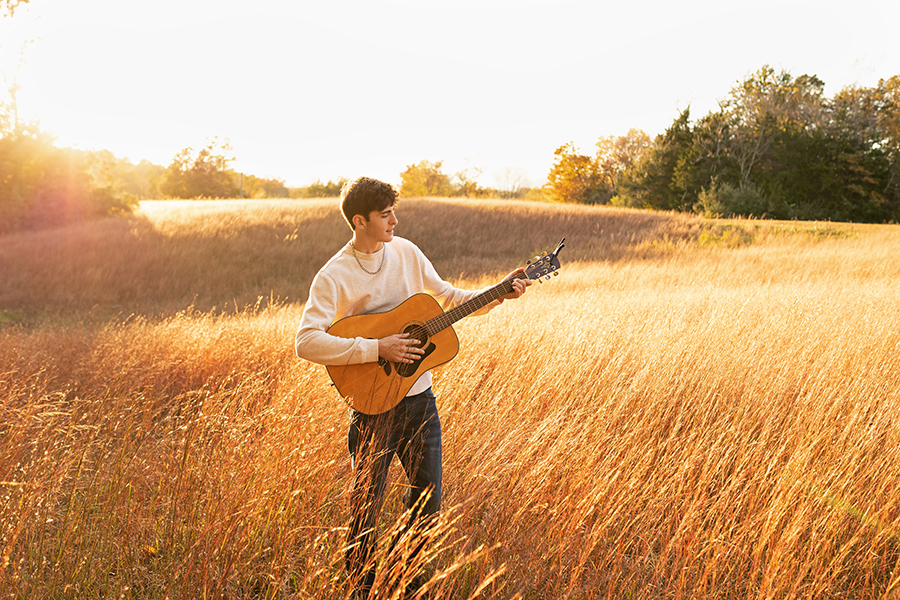 High school senior playing an acoustic guitar outdoor, highlighting scenic senior portrait locations with a Charlottesville senior photographer.