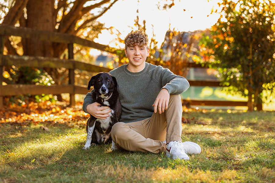 High school senior posing with his black dog during senior pictures with pets, captured by a Charlottesville senior photographer.