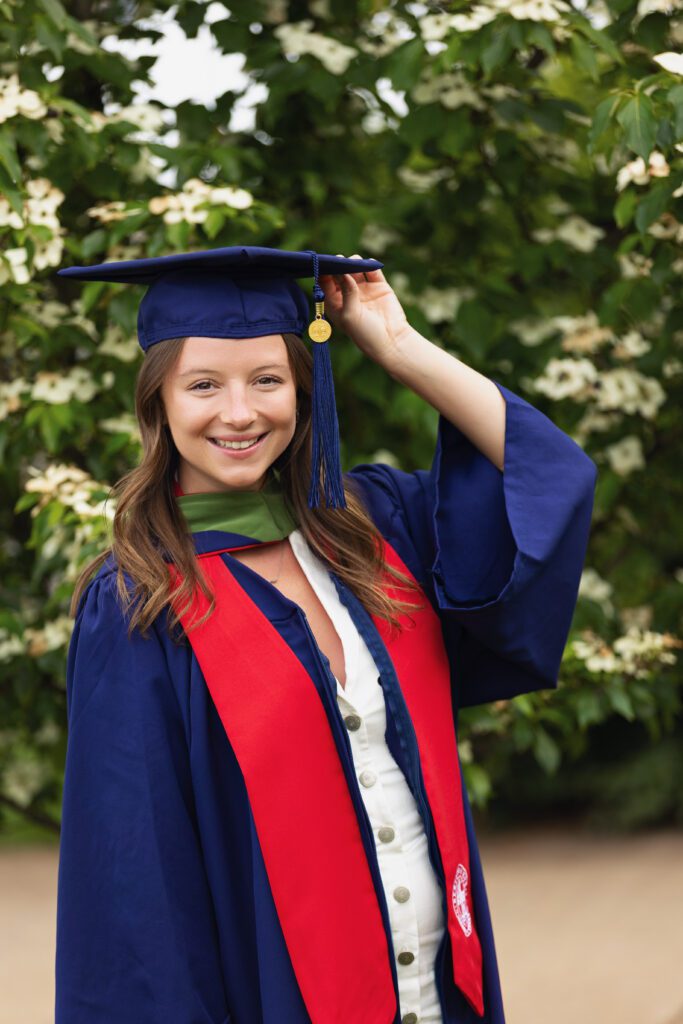 Smiling college graduate wearing a graduation cap in front of blooming trees during a senior portrait session in Charlottesville.