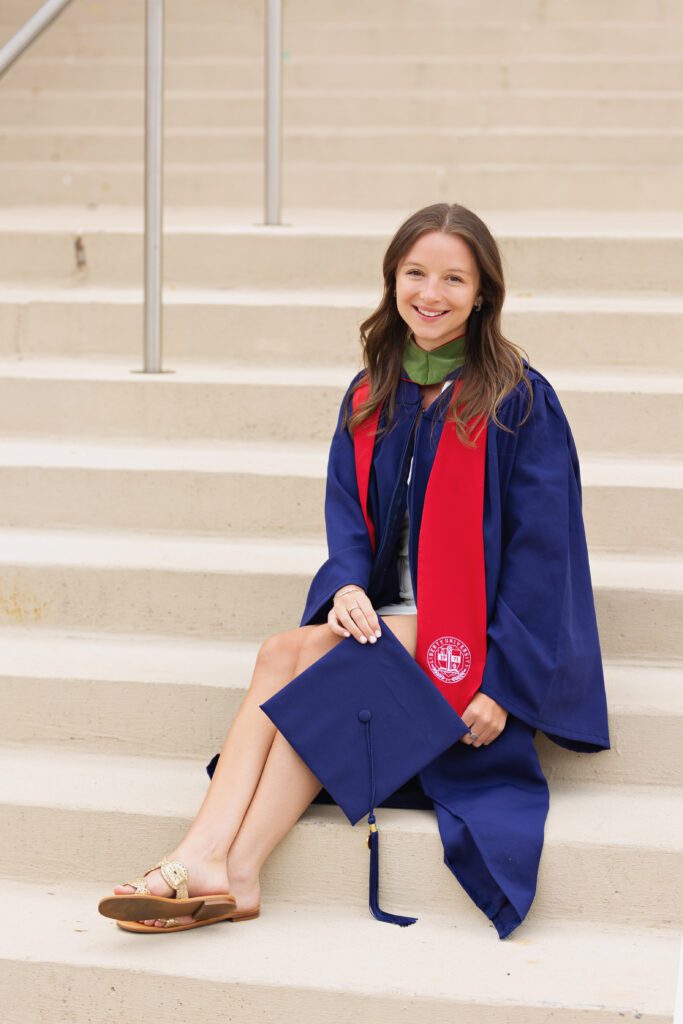 College graduate sitting on campus steps holding her graduation cap during a senior portrait session in Charlottesville, Virginia.