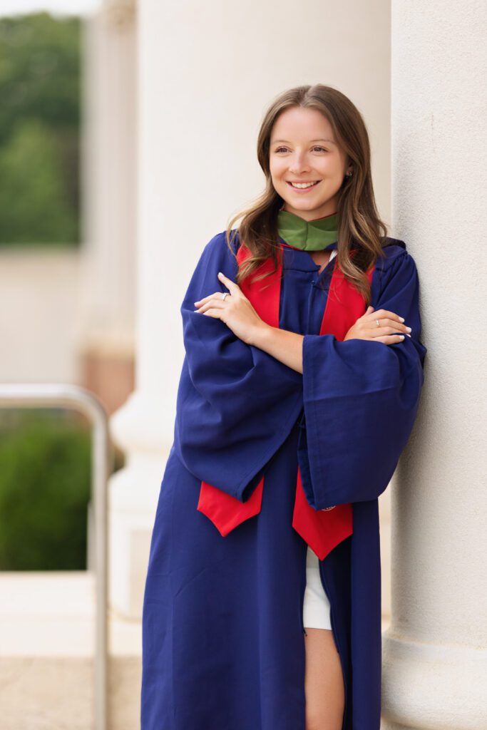 Graduate smiling while leaning against campus columns during a senior photo session with a Charlottesville Senior Photographer. Find out when to book senior pictures for your graduation portraits.