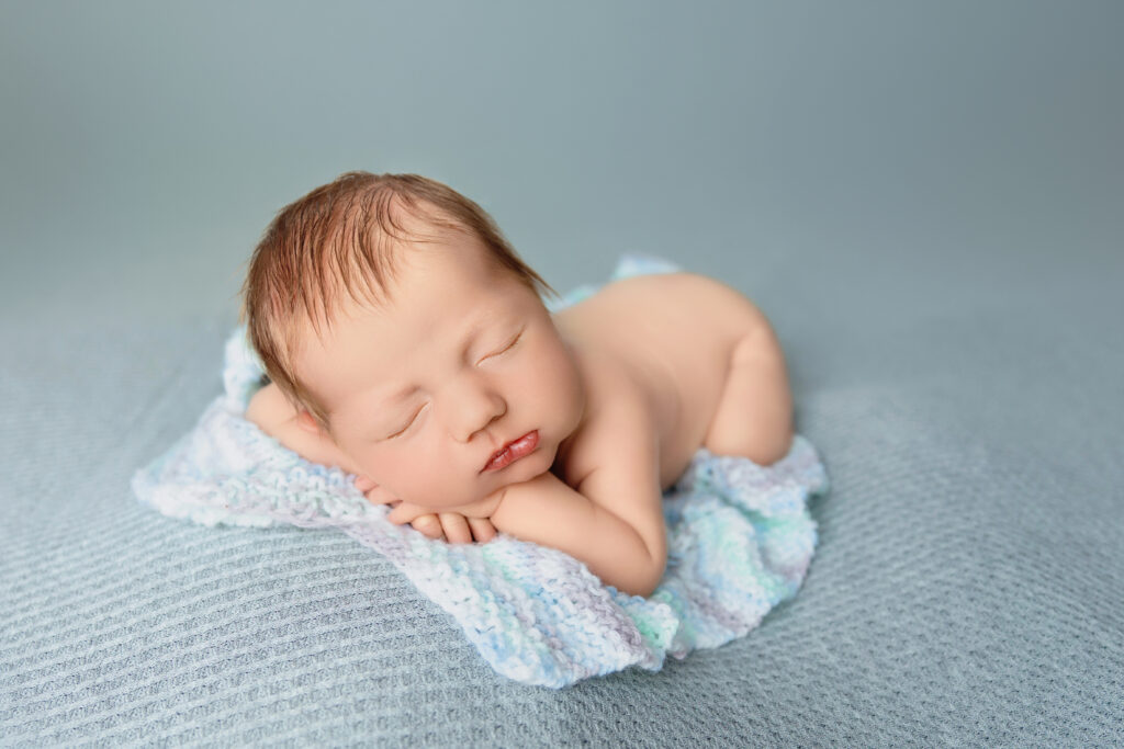 Sleeping newborn posed on a soft blue blanket in a professional studio at Charlottesville, VA.