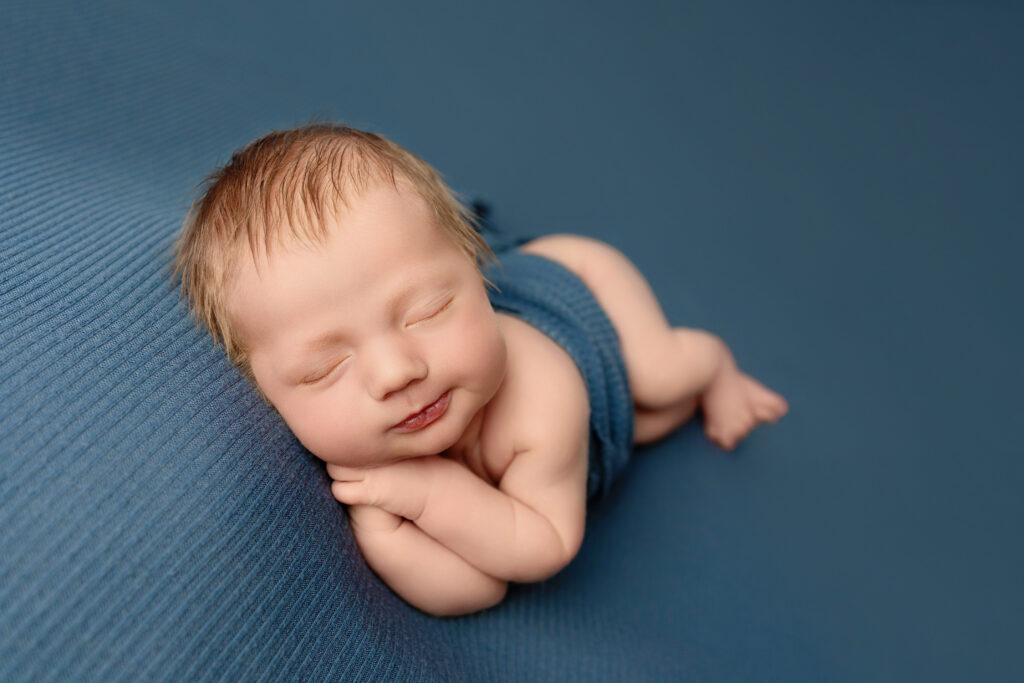 Peaceful newborn sleeping on a blue backdrop during a professional newborn portrait session.