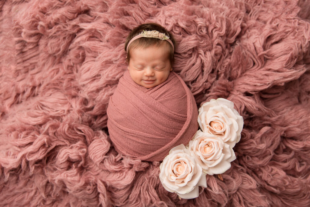Smiling newborn wrapped in pink with roses during a newborn photography studio session. Captured by Charlottesville newborn photographer - Amy Yang Photography.