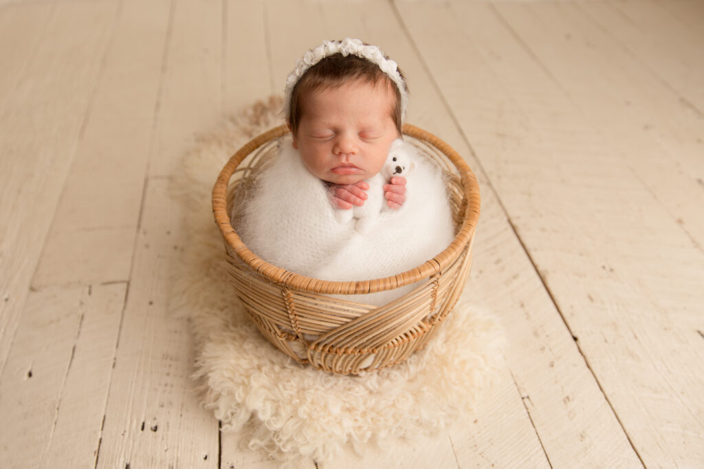 Newborn wrapped in white posing in a basket at a newborn photography studio.