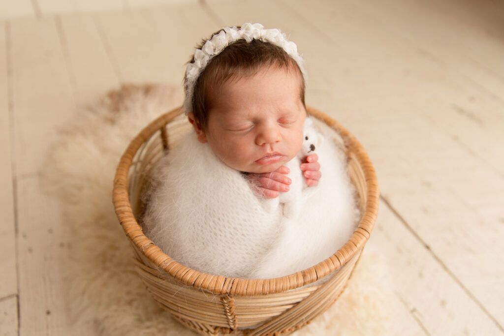 Close-up of a newborn wrapped in white holding a teddy bear in a photography studio. Captured by a Charlottesville newborn photographer - Amy Yang Photography.