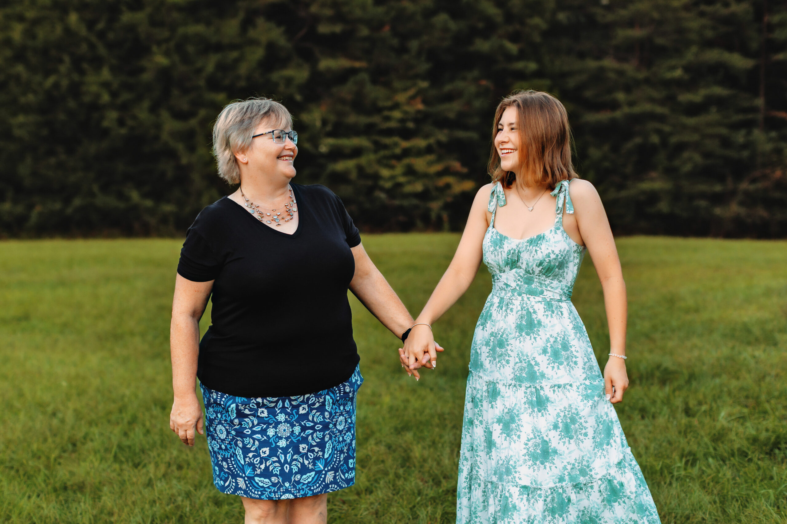 Mother and high school senior holding hands in a grassy field, capturing family photos with senior portraits by a senior photographer in Richmond, VA.