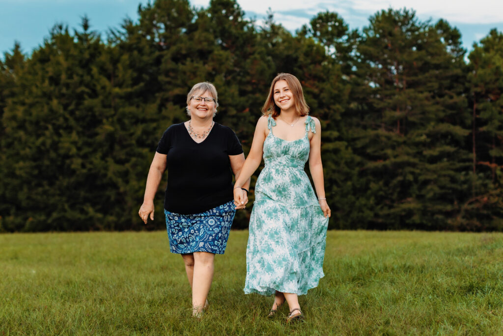Mother and graduating senior walking hand in hand through an open field, combining family photos with senior portraits during a Richmond, Virginia senior photography session.