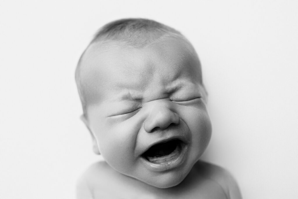 Crying newborn portrait capturing a joyful expression during a heirloom newborn photography session.