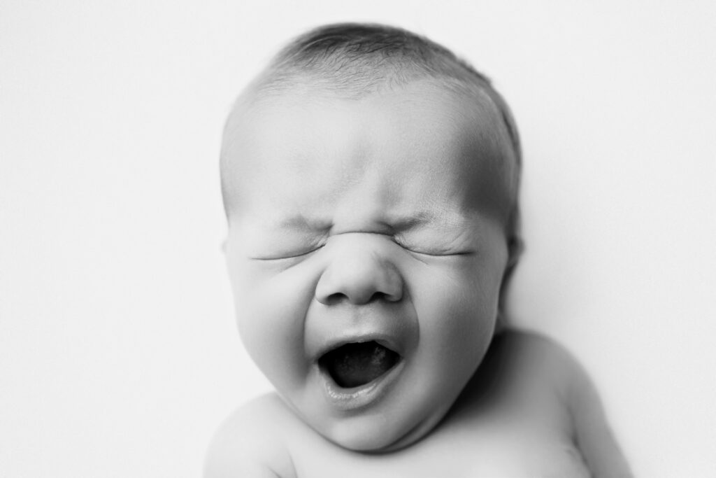 Yawning newborn captured in a classic heirloom newborn photography portrait with natural expression.