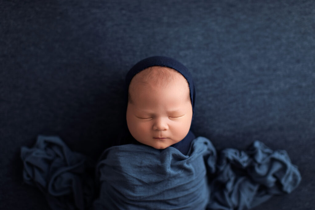 Wrapped sleeping newborn in a navy blue wrap during a luxury newborn photography session in Charlottesville, VA.