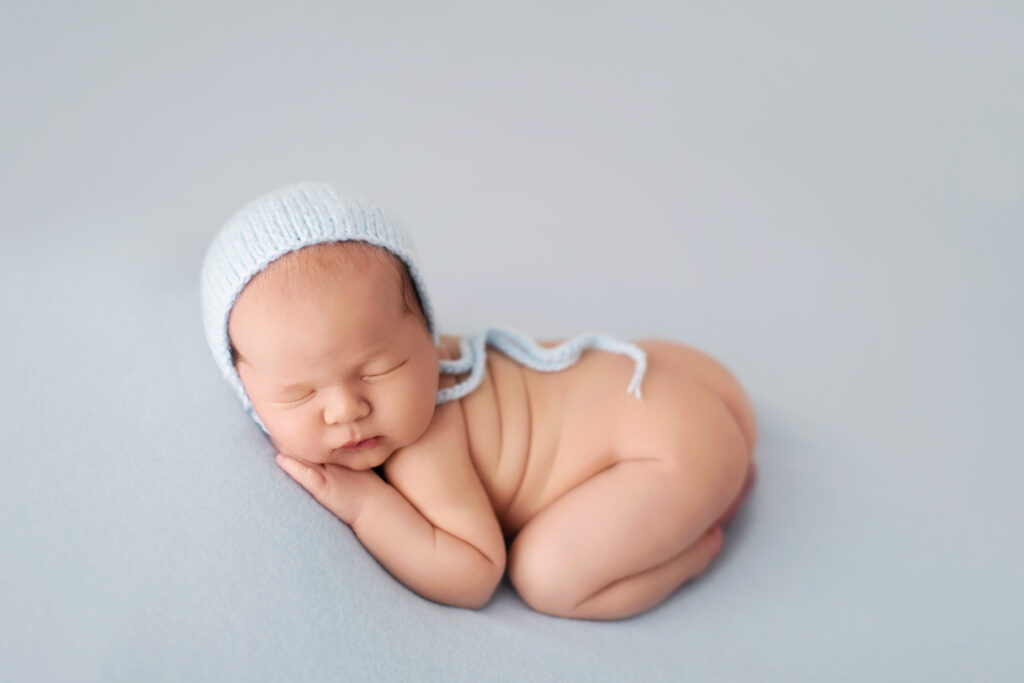 Sleeping newborn wearing a light blue knit bonnet in a classic side pose for a luxury newborn photography session.