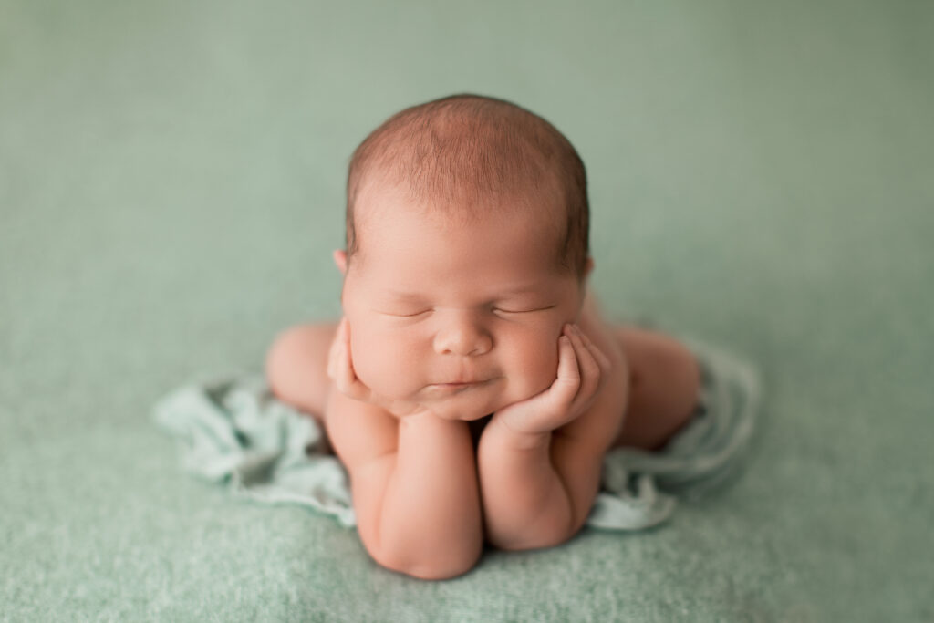 Charlottesville luxury newborn photography featuring a sleeping baby posed with hands supporting the chin on a soft mint backdrop.