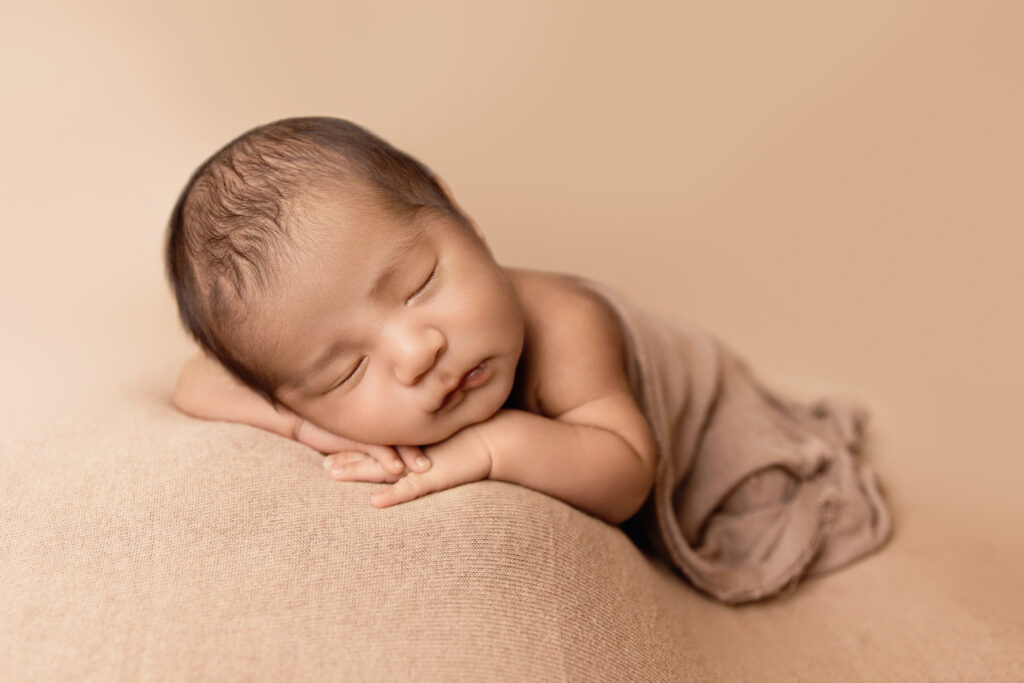 Peacefully sleeping newborn posed on a soft beige backdrop by a newborn photographer Earlysville VA.