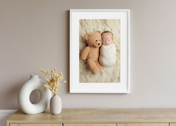 Framed newborn portrait wall art featuring a sleeping baby and teddy bear in a nursery by Amy Yang Photography.