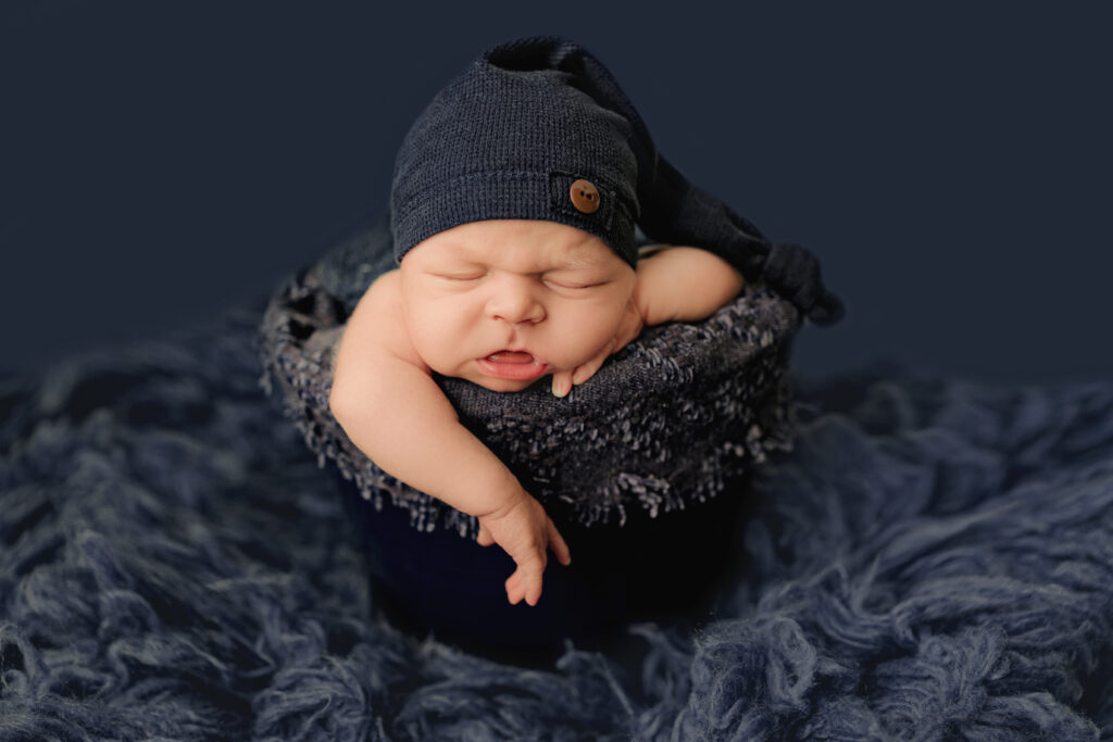 Newborn photographer Crozet VA capturing a sleeping baby in a navy knit hat posed peacefully in a cozy bucket.