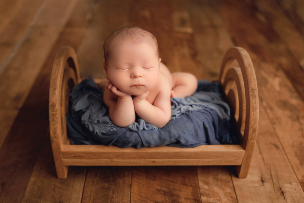 Newborn photos as home decor featuring a baby posed on a wooden bed with blue blankets by Charlottesville newborn photographer.