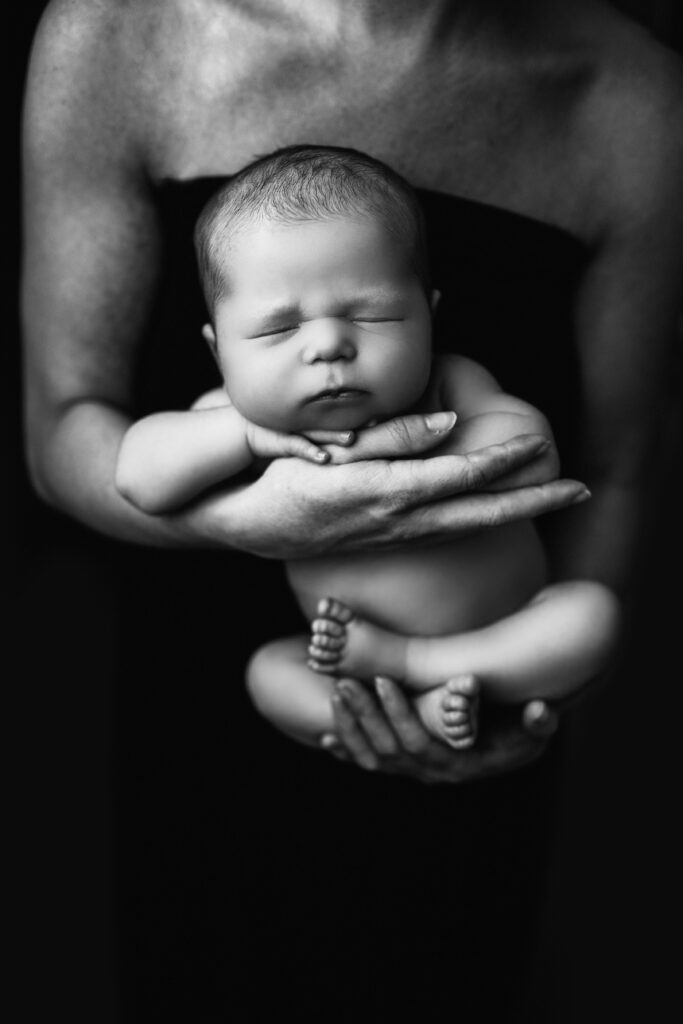 Black and white newborn photos as home decor showing a sleeping baby cradled in a parent's hands.