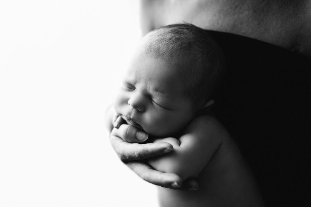 Black and white newborn photos as home decor of a sleeping baby resting in a parent's hand.