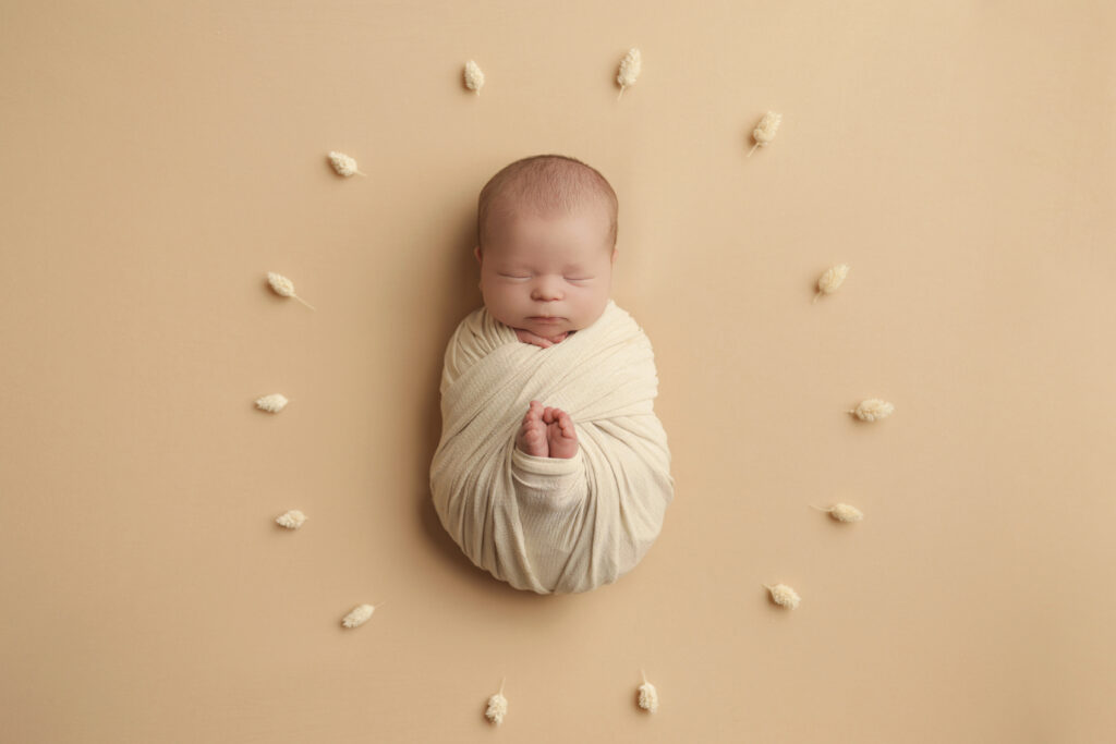 Minimalist newborn photos as home decor with a wrapped baby on a soft cream background.