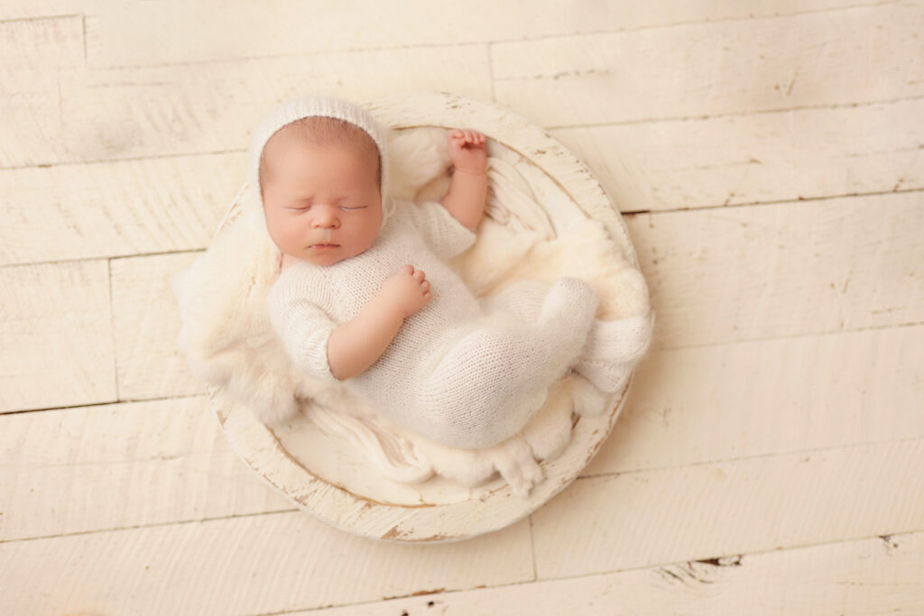 Elegant newborn photos as home decor of a sleeping baby in a white knit outfit and bowl prop.