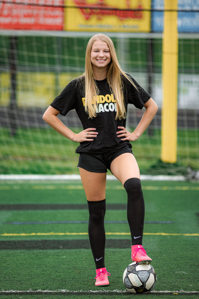Varsity soccer player posing with a soccer ball on the field during a senior session with a senior photographer in Richmond, VA.
