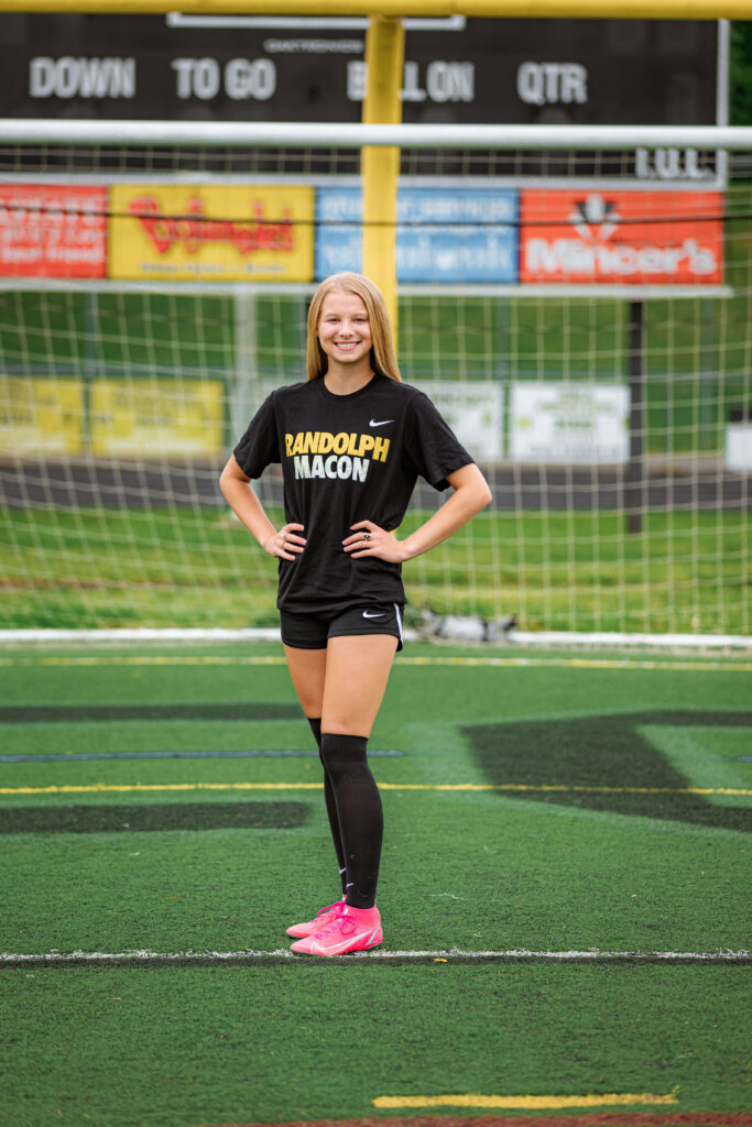 High school soccer player in a Randolph-Macon training outfit standing confidently on the field, highlighting outfit changes for senior pictures during a senior portrait session.