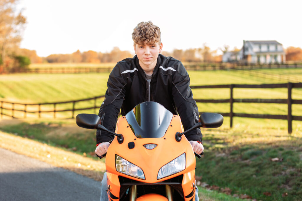 Confident high school senior posing on an orange sport motorcycle during a golden hour senior portrait session in rural Charlottesville, VA,