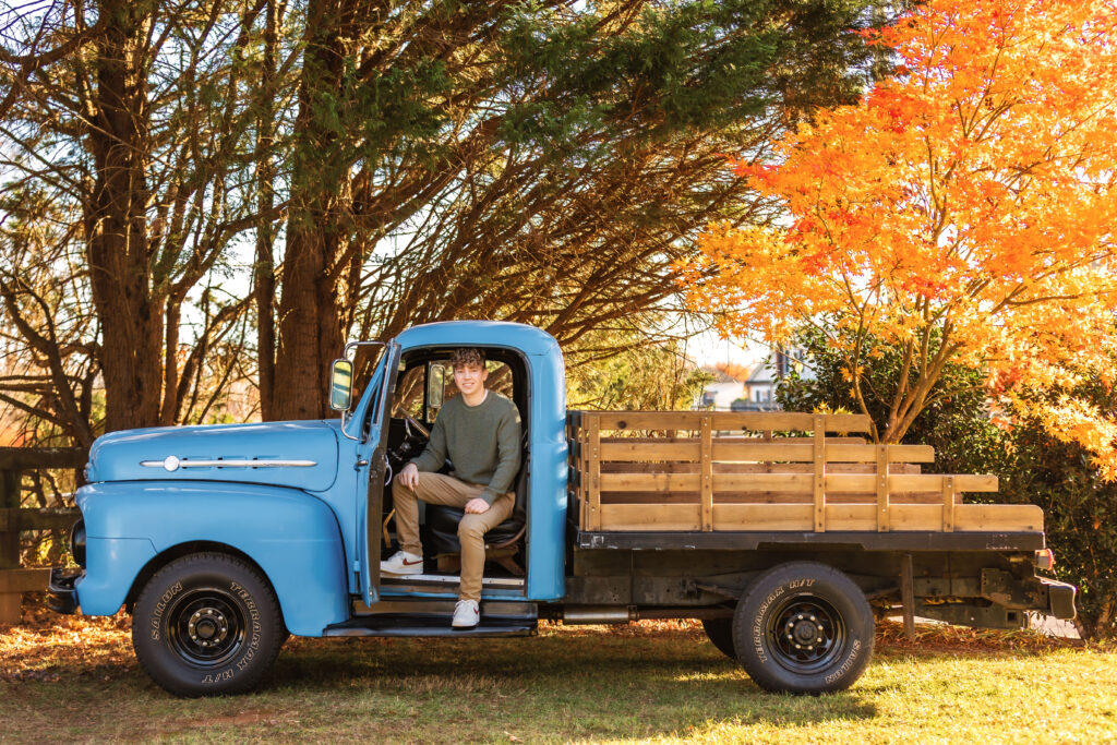 Senior boy posing in a vintage blue truck during a personalized outdoor session, highlighting senior pictures for guys by a Charlottesville Senior Photographer.