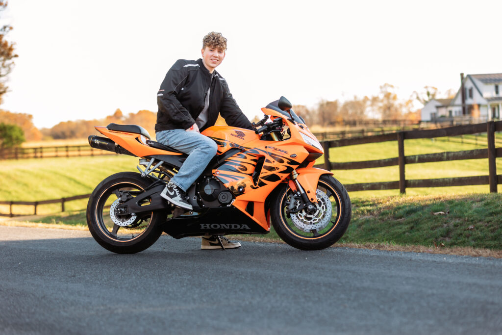 High school senior sitting on an orange sport motorcycle during an outdoor portrait session, showcasing senior pictures for guys with a Charlottesville Senior Photographer.