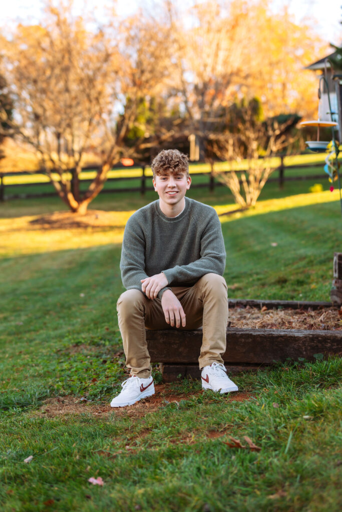 Smiling high school senior sitting on a wooden garden during senior session in Virginia.