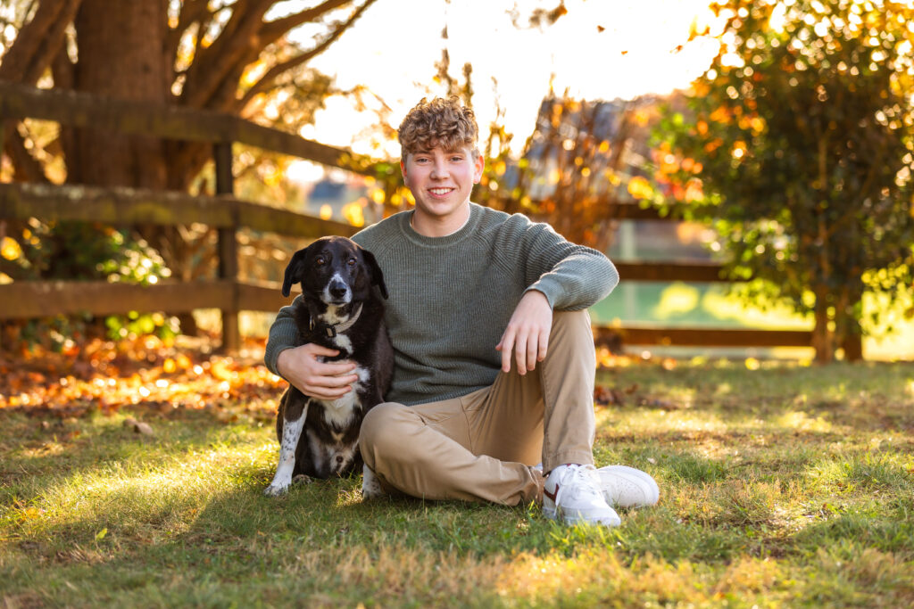 High school senior posing with his black dog during senior pictures with pets, captured by a Charlottesville senior photographer.