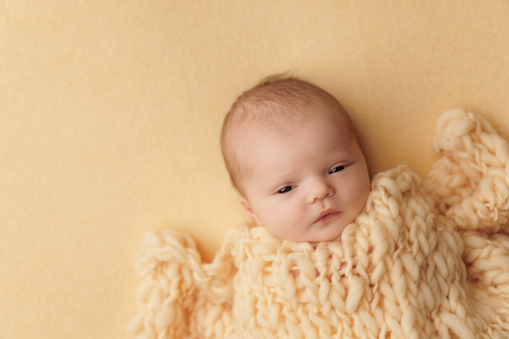 Awake newborn wrapped in a chunky cream knit blanket during a newborn photography session in Charlottesville, VA.