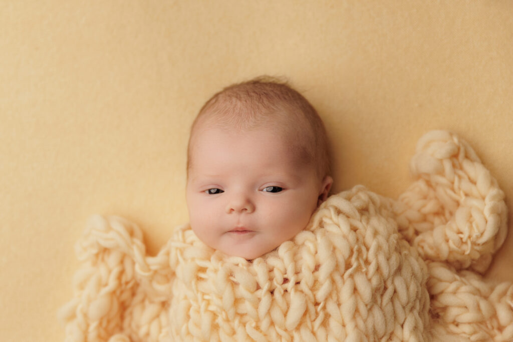 Newborn baby looking at the camera in a cream knit wrap.
