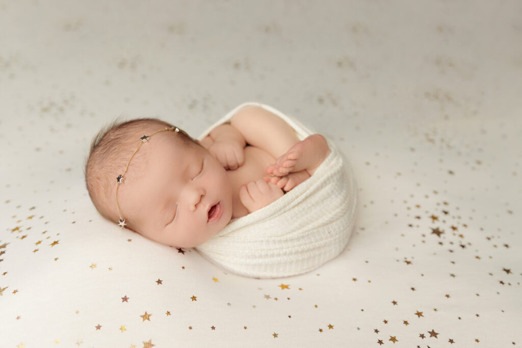 Sleeping newborn wrapped in a white swaddle on a star blanket.